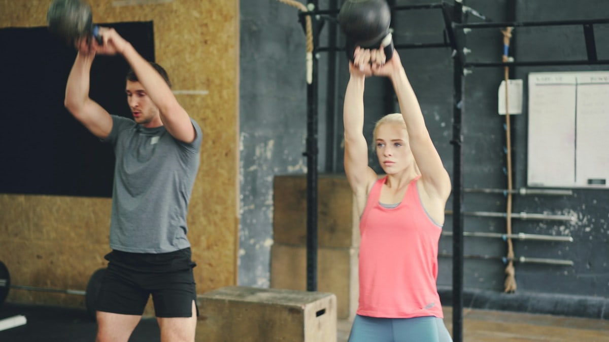Young woman and man are working out with heavy dumbbells squatting and lifting weight exercising indoors in modern sports gym. People and lifestyle concept.